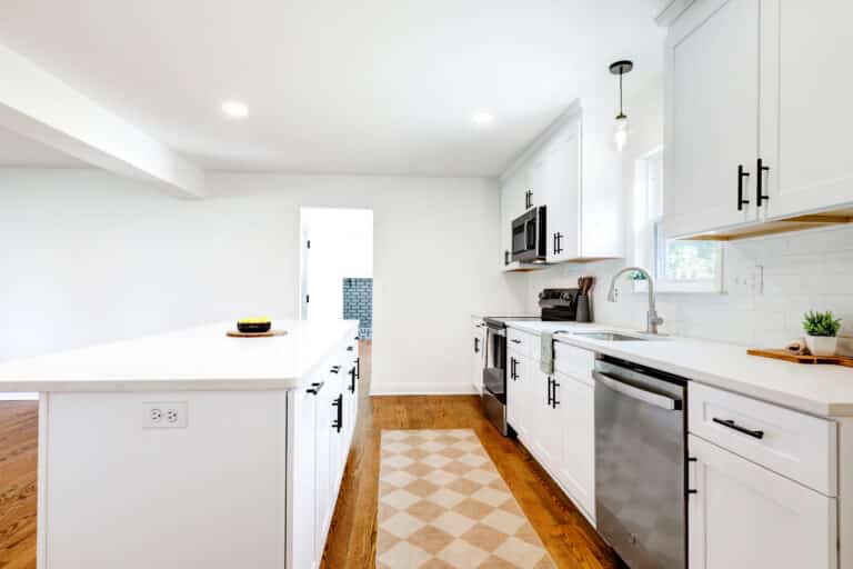 Wood flooring along the aisle between white kitchen cabinets and an island