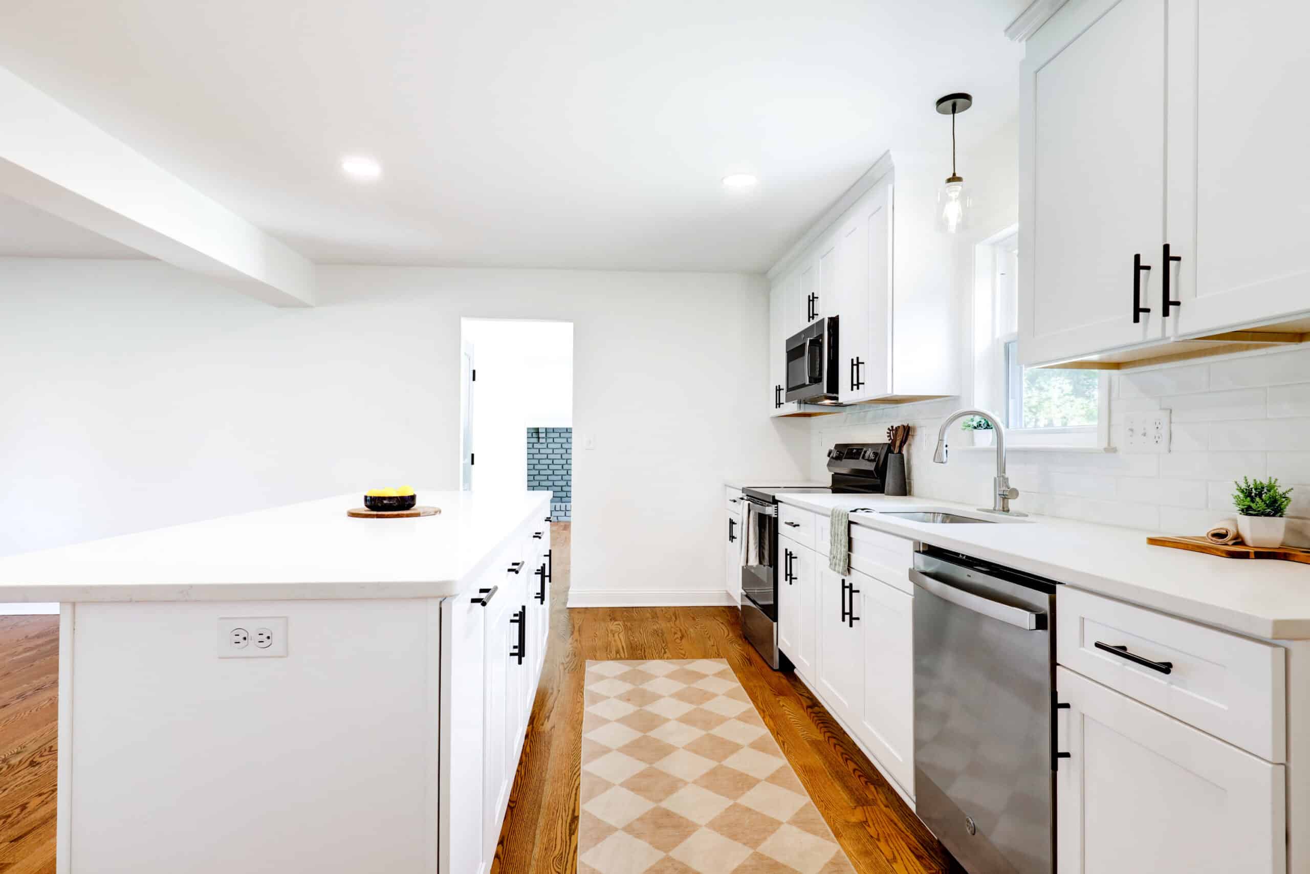 Wood flooring along the aisle between white kitchen cabinets and an island